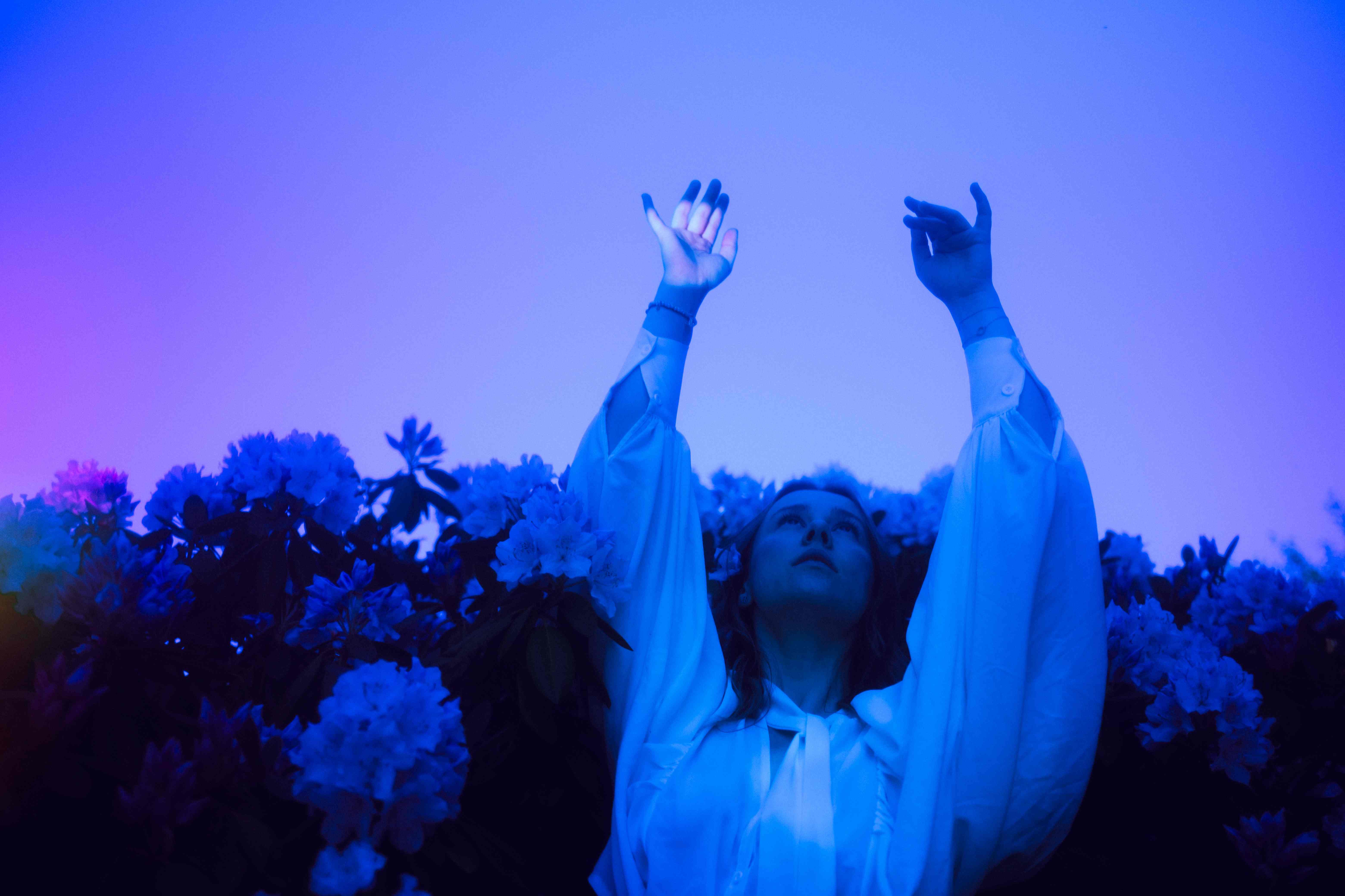 Person with arms raised toward the sky in blue-purple lighting