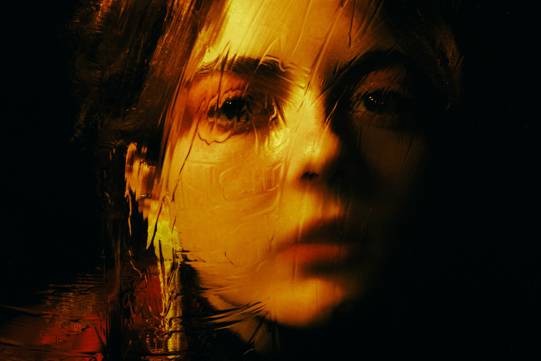 Portrait lit in warm amber light behind textured wet glass