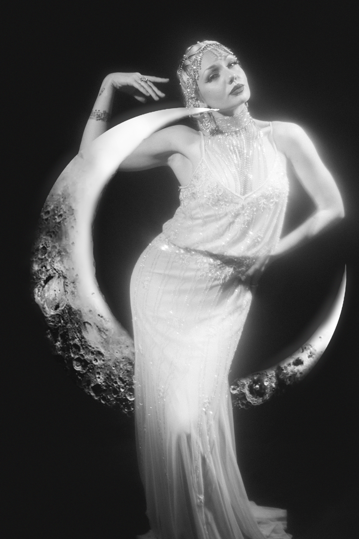 Black and white portrait of a performer in a beaded gown against a glowing crescent moon