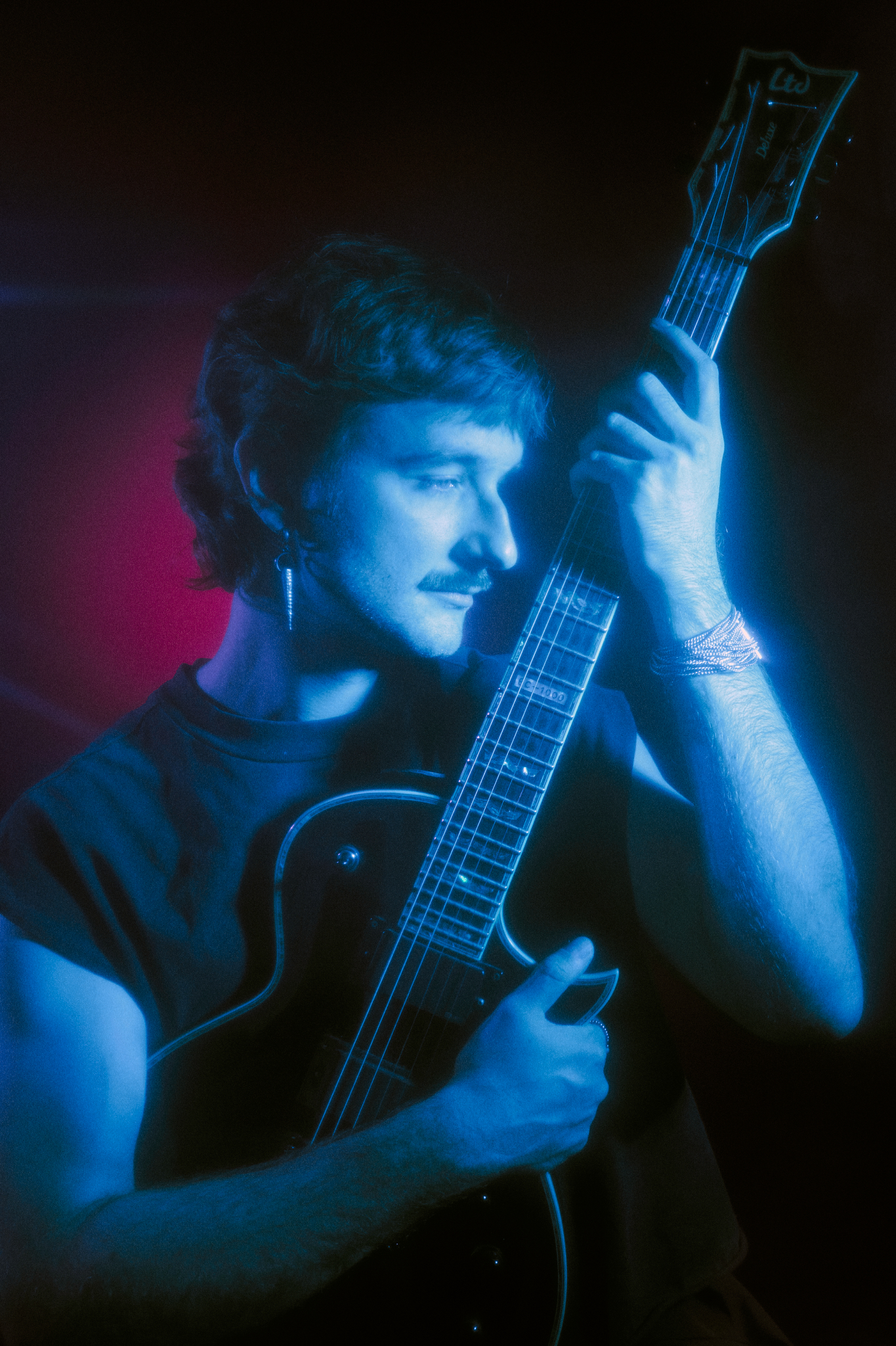 Close portrait of a guitarist lit in deep blue, resting against the neck of the guitar